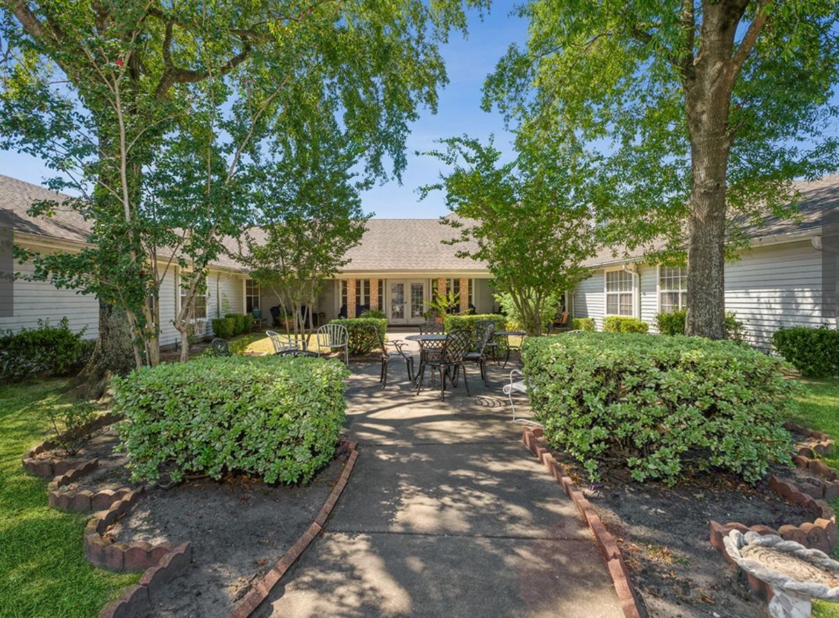 A charming house with a well-maintained garden and outdoor seating, surrounded by lush trees and greenery.