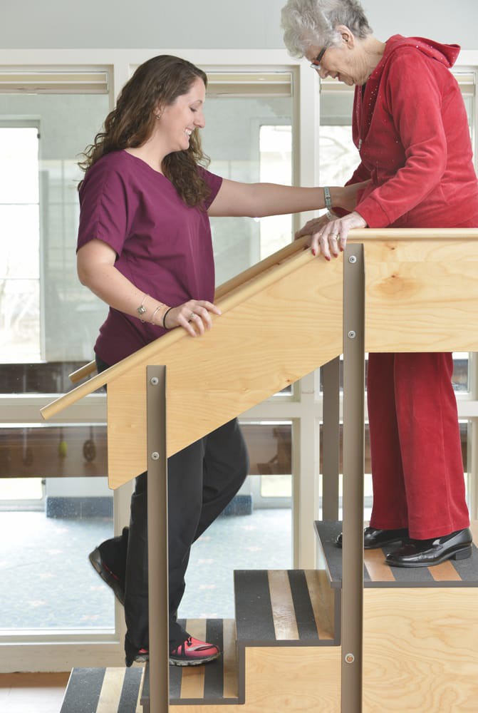 A physical therapist assists a patient with stair climbing exercises in a rehabilitation setting.