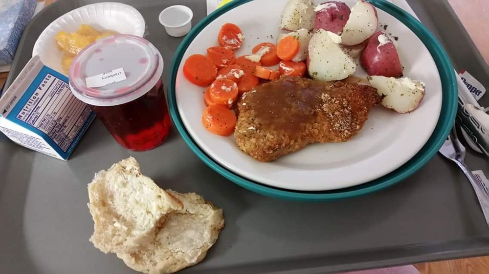 A meal on a tray featuring chicken, potatoes, carrots, bread, and a drink.