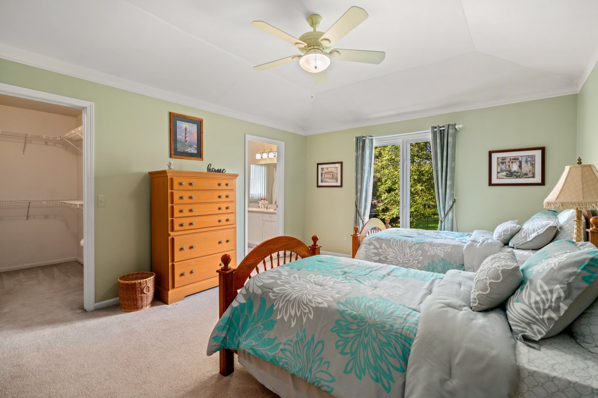A cozy bedroom featuring twin beds with floral bedding, a wooden dresser, and a ceiling fan.