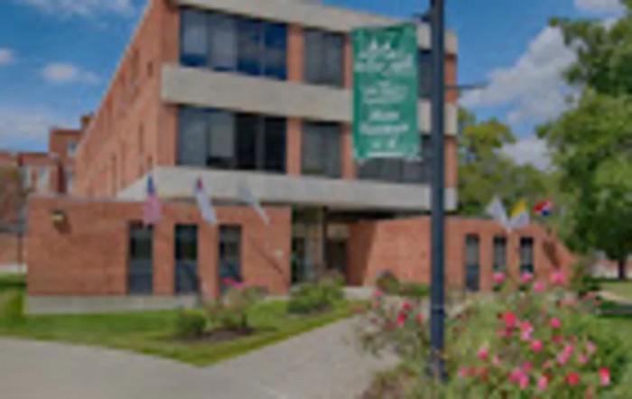 A brick building with a garden in front and several flags displayed, along with a banner on a pole.