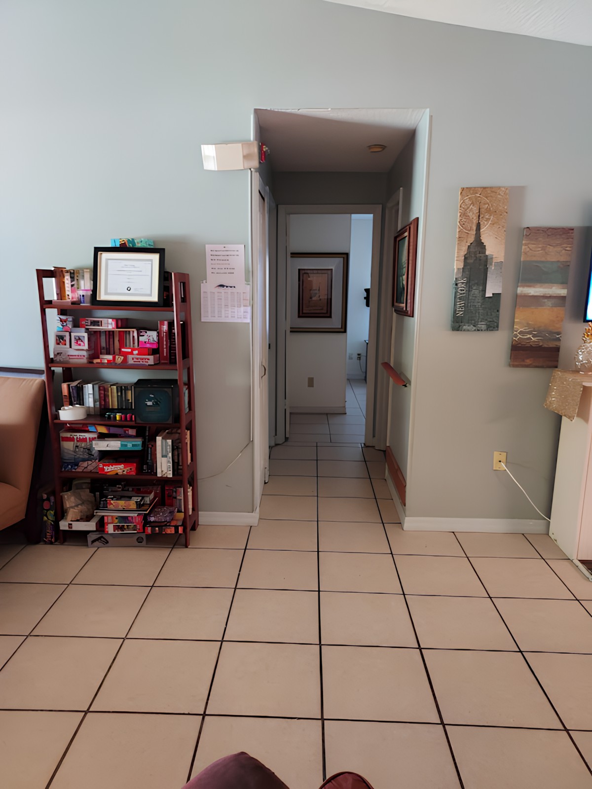A view of a waiting room with a hallway, featuring a bookshelf and artwork on the walls.