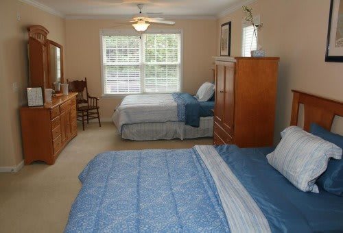 A spacious bedroom with two beds, a dresser, and large windows.