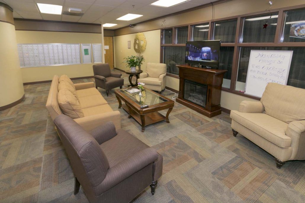 A cozy living room with sofas, chairs, a coffee table, a television above a fireplace, and ample lighting.