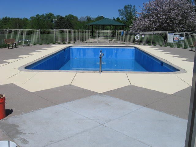 An outdoor swimming pool on a clear day, surrounded by trees and open space.