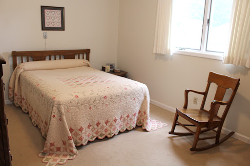 A cozy and minimalist bedroom featuring a bed with a decorative blanket and a rocking chair by the window.