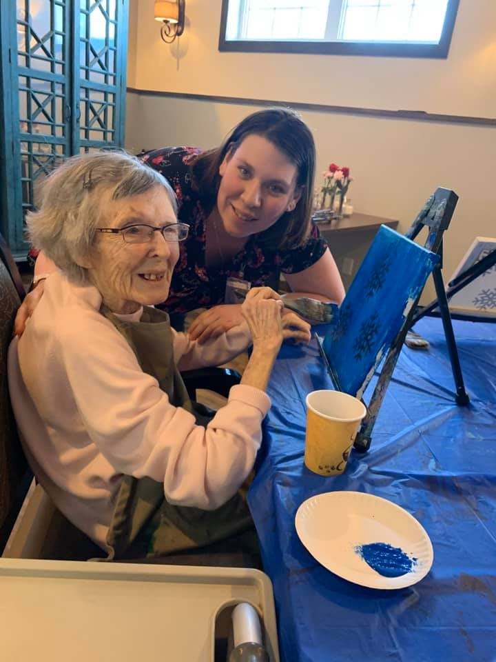 An elderly woman enjoying an art class with a companion.