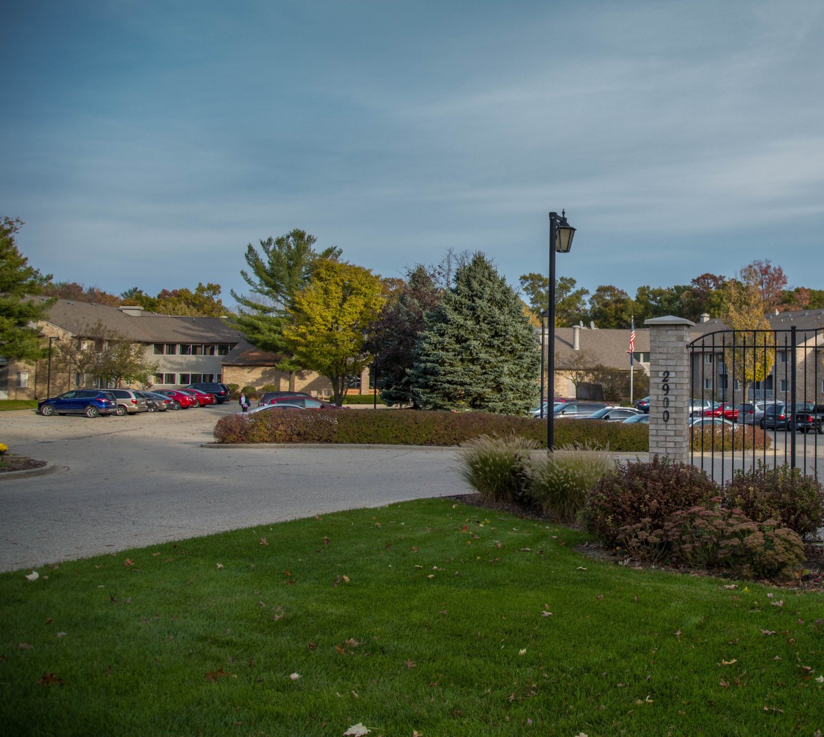 A suburban parking lot surrounded by trees and buildings under a cloudy sky.
