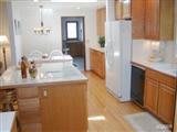 A modern kitchen with wooden cabinets and a central island, featuring bright lighting and spacious design.