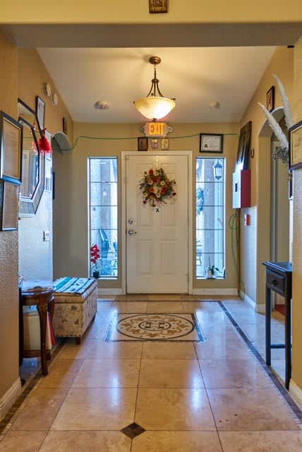 A cozy entryway featuring a front door adorned with a wreath, flanked by windows and warm lighting.