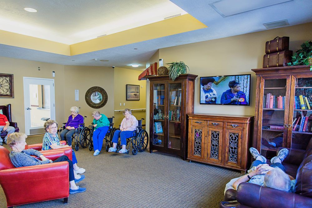 A group of elderly people in wheelchairs watching television in a communal living room.