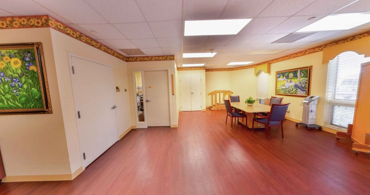 A spacious office interior featuring a meeting area with a table and chairs, wood flooring, and ceiling lights.