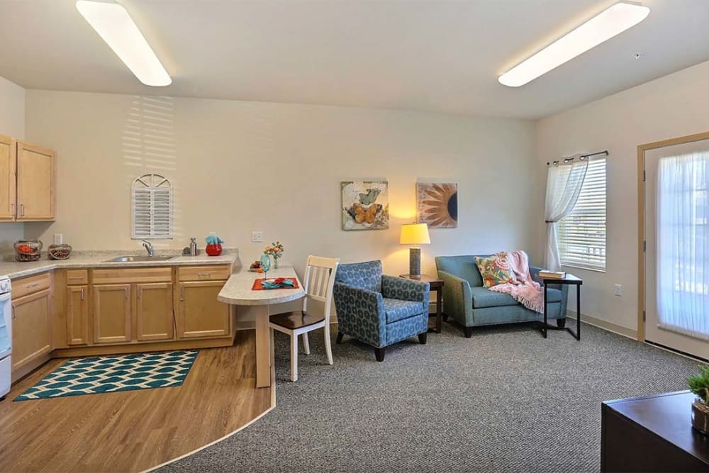 A cozy living space with a kitchenette, featuring two armchairs, a table, and decorative elements.