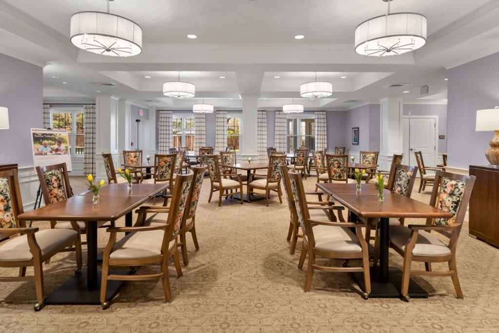 A spacious dining room with arranged tables and chairs under elegant chandeliers.