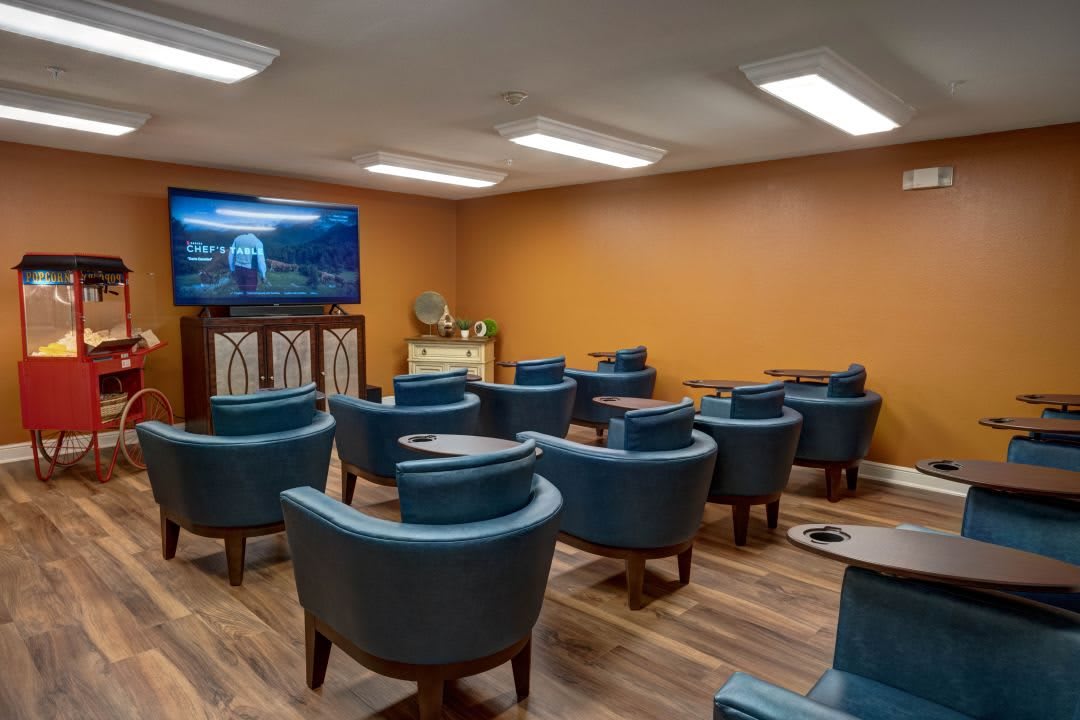 A small theater room with blue chairs facing a large TV on an orange wall.