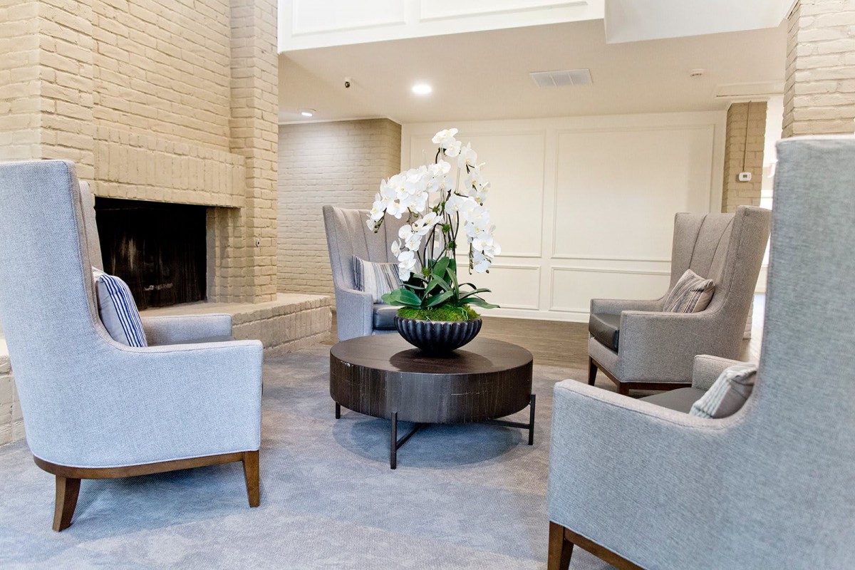 A modern lobby featuring comfortable seating around a fireplace, with a central coffee table adorned with an orchid plant.