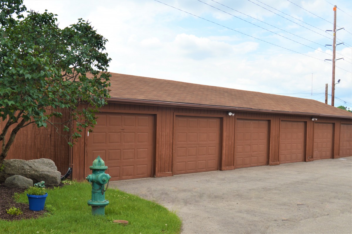A row of garage doors with a fire hydrant and tree nearby.