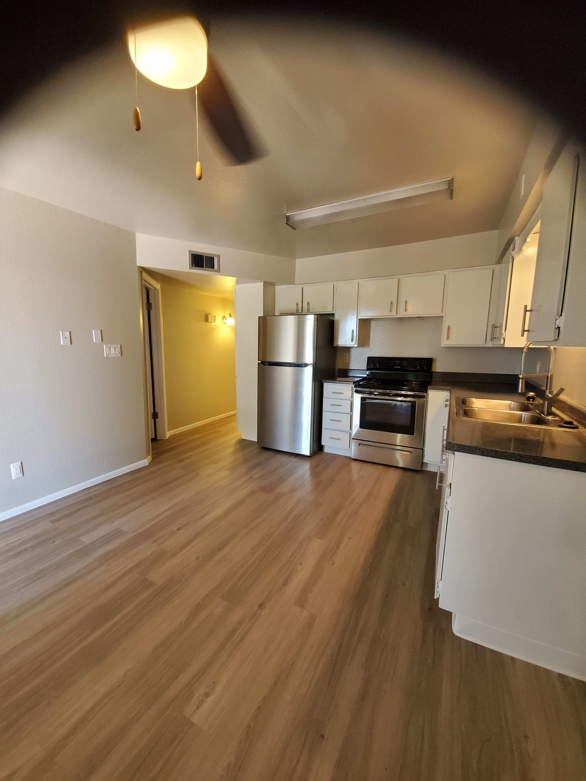 A modern apartment kitchen with stainless steel appliances and wooden flooring.