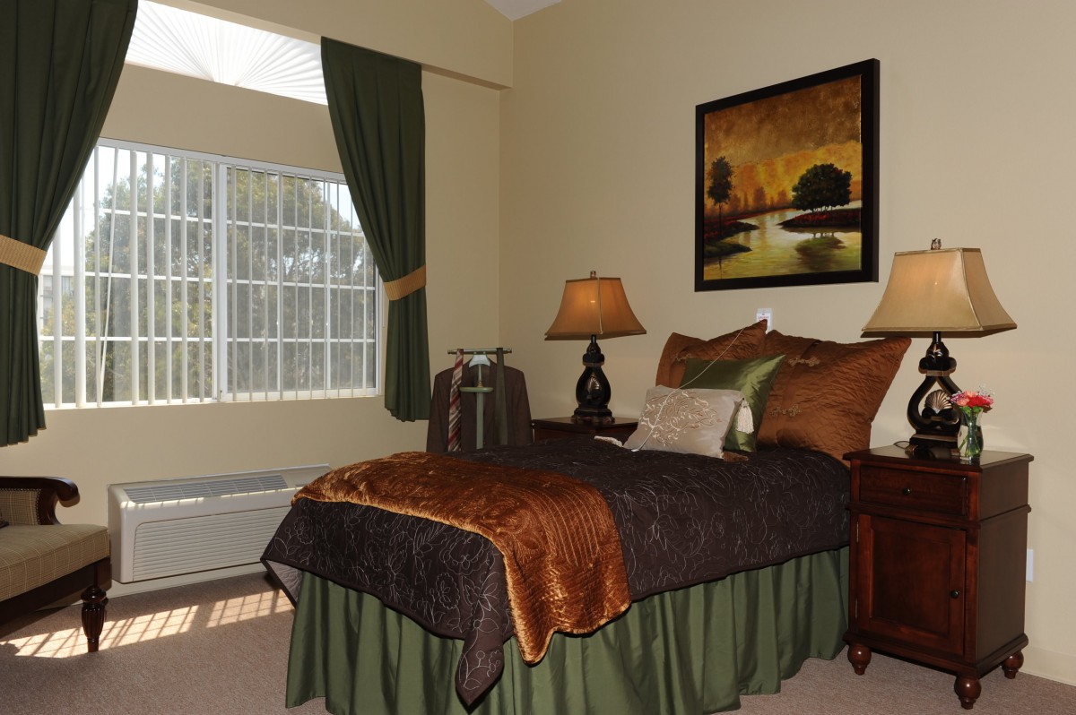 A cozy bedroom with warm tones, featuring a neatly made bed, bedside lamp, and decorative painting.
