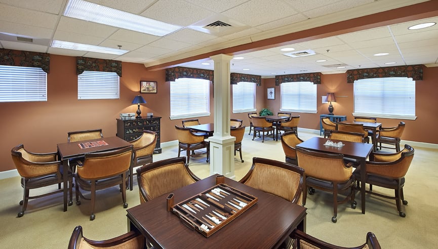 A cozy recreation room with multiple tables and chairs, featuring a chess board on one of the tables.