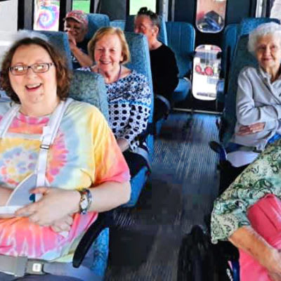 A group of people smiling while sitting on a bus.