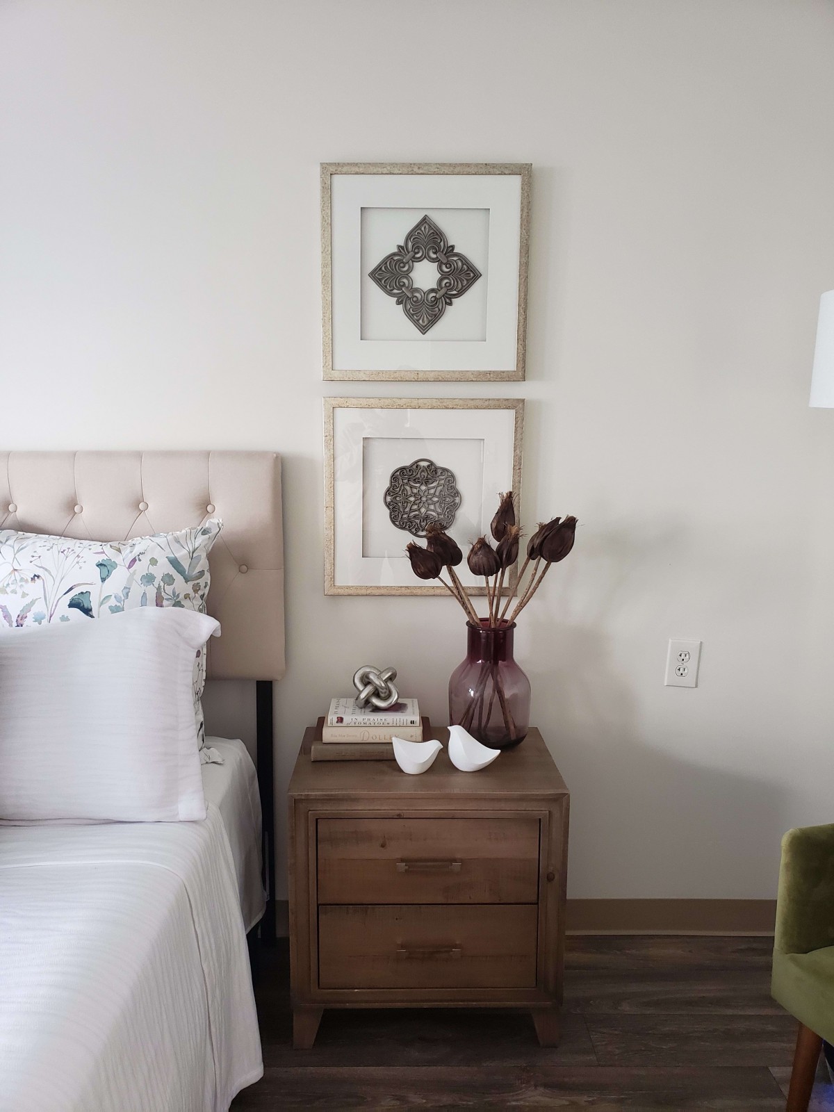 A minimalist bedroom with a wooden nightstand, decorated with a vase and wall art.