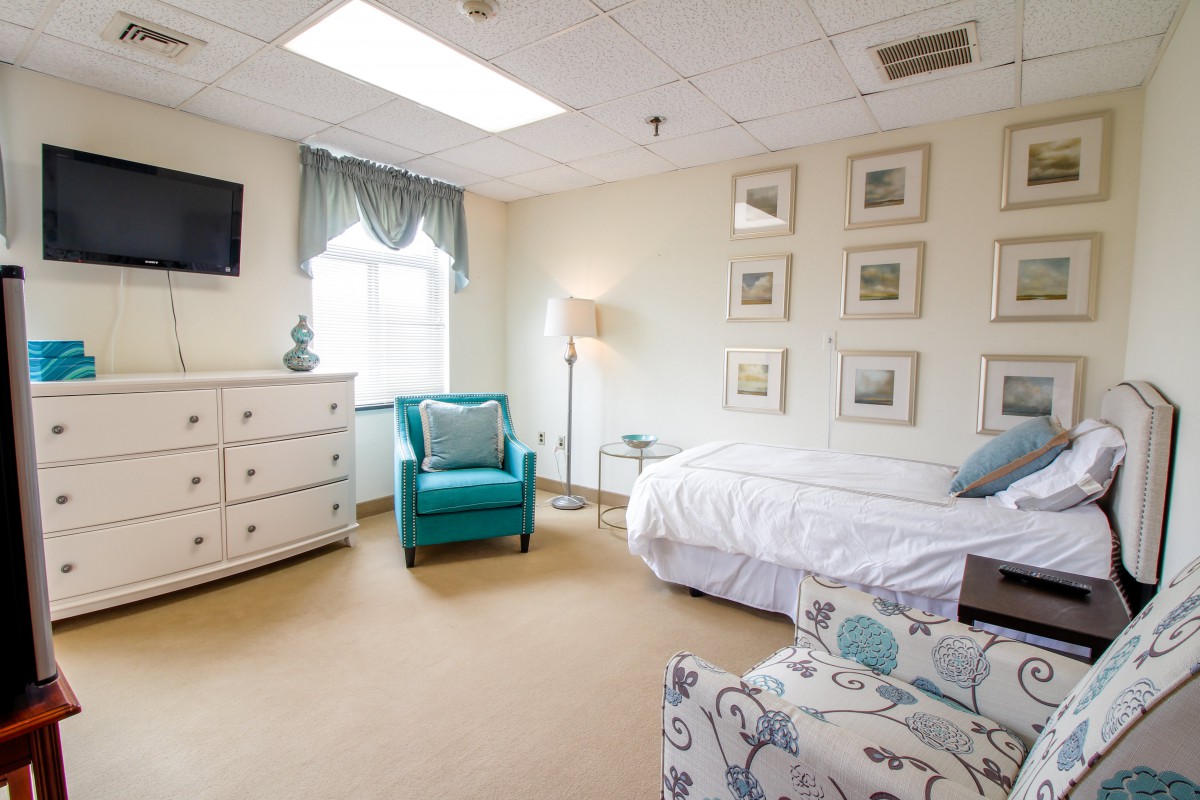 A cozy and well-decorated bedroom with a bed, teal armchair, dresser, and wall art.