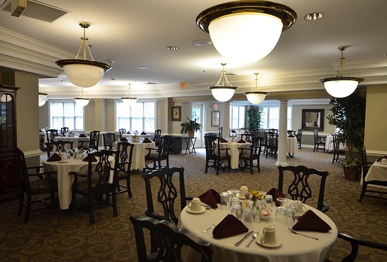 An elegant dining room with round tables set for service, featuring chandeliers and classic decor.