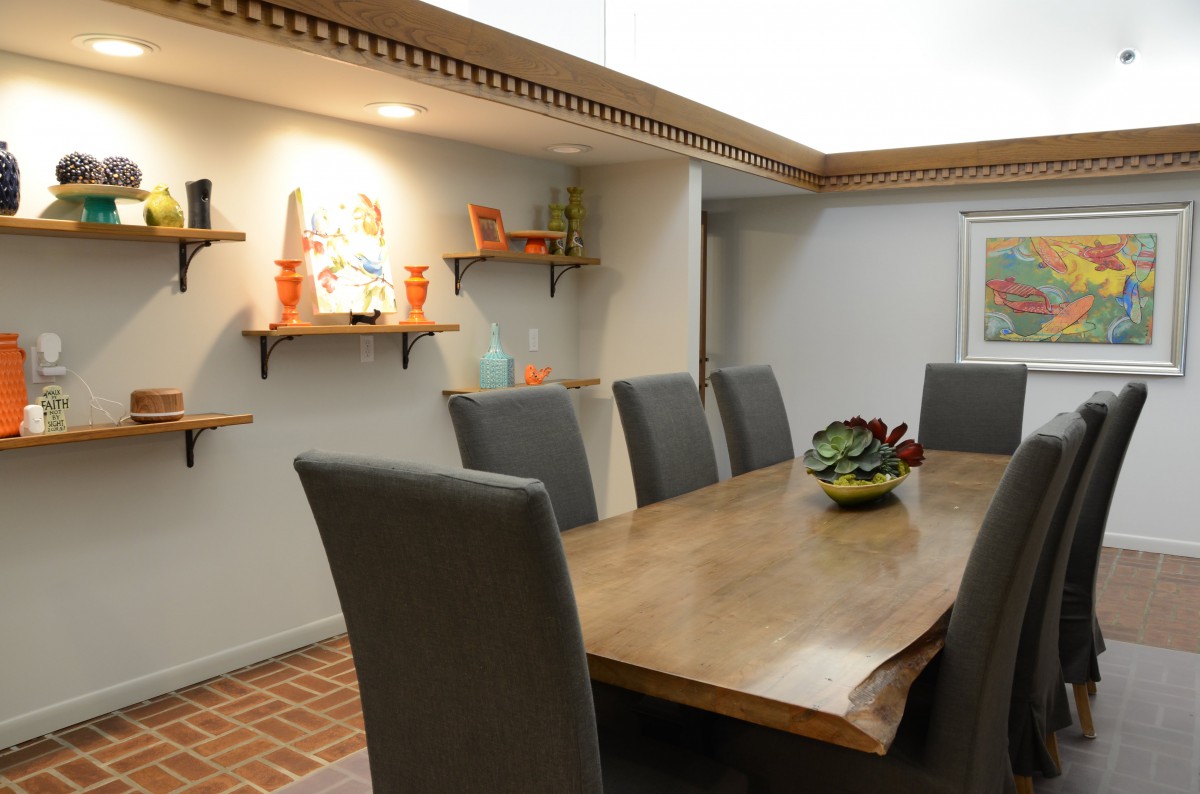 A modern dining room with a wooden table and gray chairs, featuring decorative shelves on the wall.