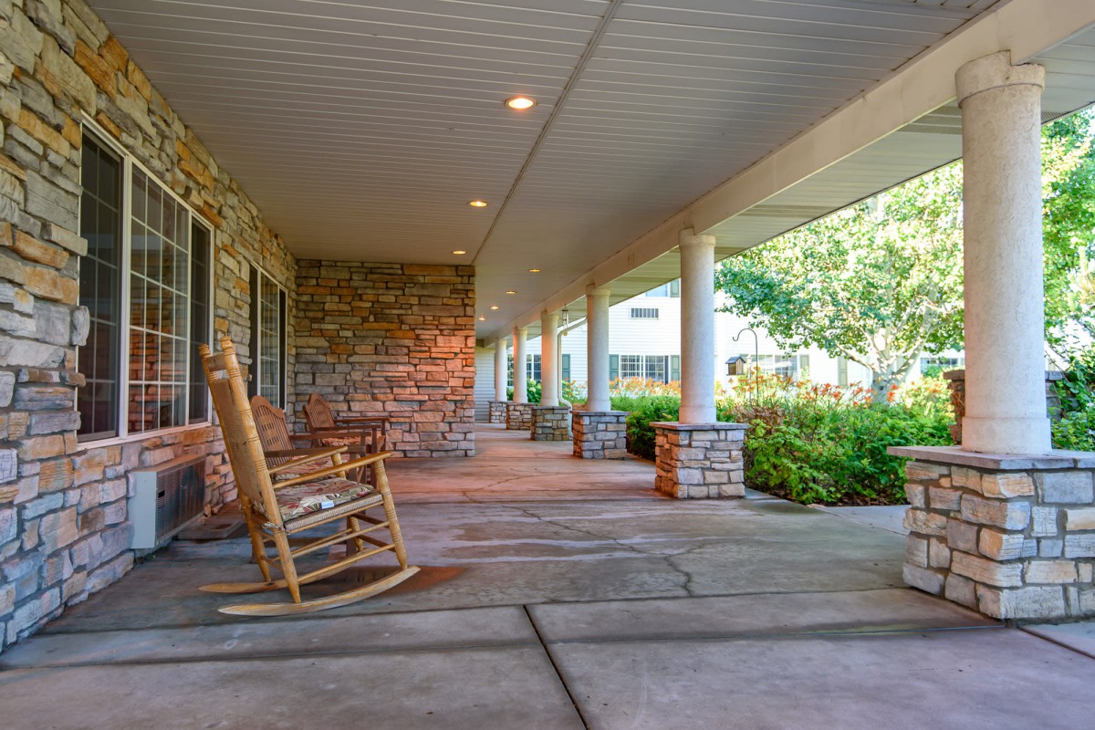A peaceful porch with a wooden rocking chair, surrounded by columns and a lush garden.