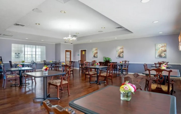 An empty dining room with wooden floors, tables, and chairs, decorated with flowers.
