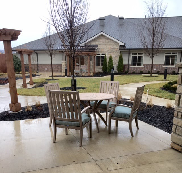 A patio with wooden chairs and a table overlooking a landscaped garden area in front of a modern building.