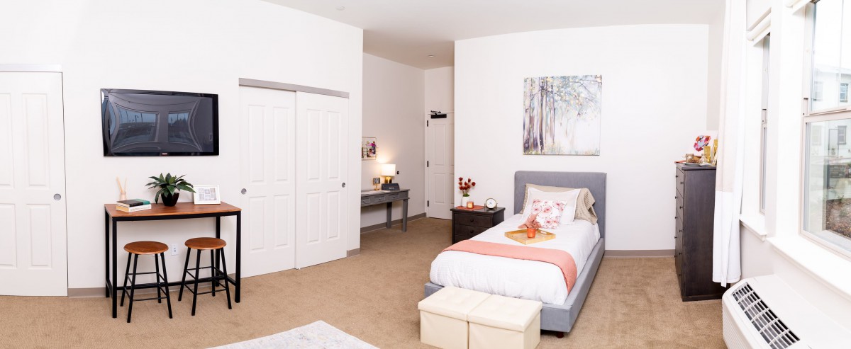 A minimalist bedroom with modern decor, featuring a single bed, nightstand, desk, and artwork on the wall.