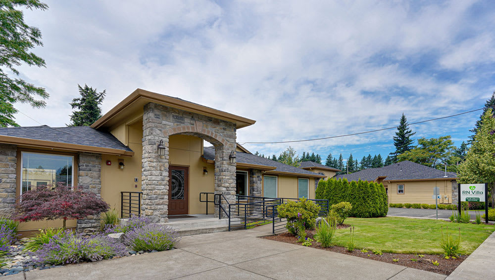 A modern house with a stone entrance and well-maintained front yard under a cloudy sky.