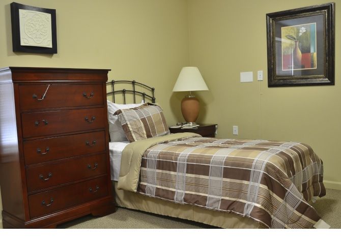 A cozy bedroom with a single bed, a wooden dresser, and a bedside lamp.