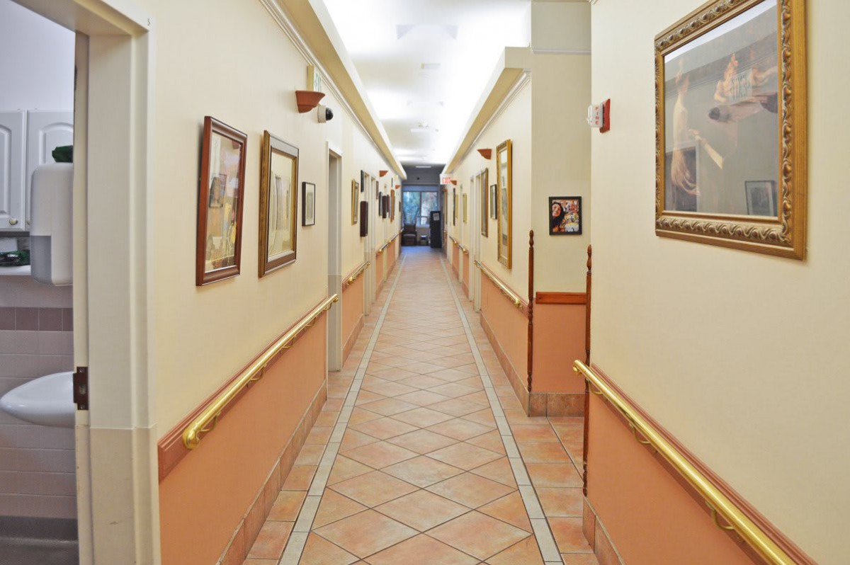 A brightly lit hallway with framed artwork on the walls and tiled flooring.