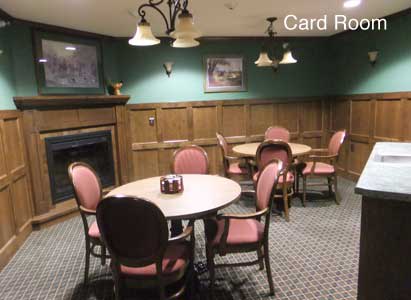 A cozy card room with round tables, chairs, and a fireplace.