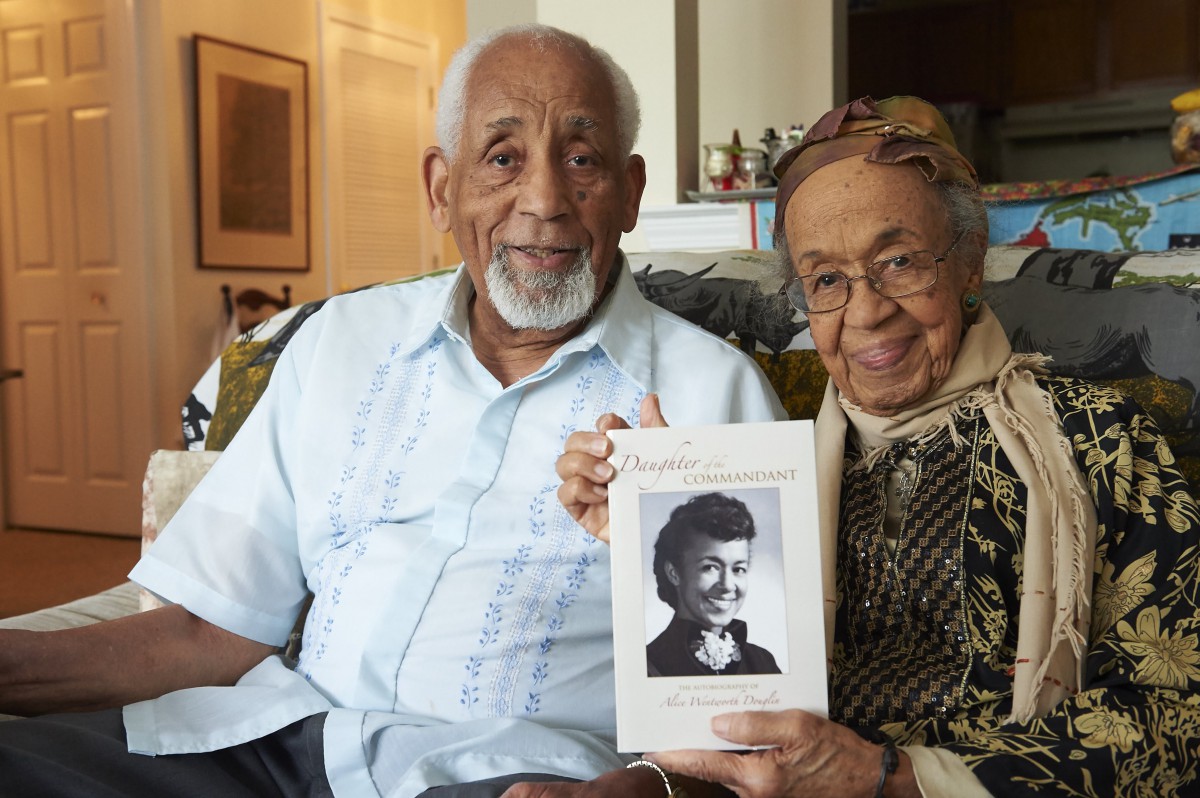An elderly couple smiles while holding a book indoors, showcasing their togetherness.