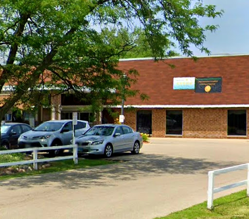 A view of an office building surrounded by trees and parked cars on a sunny day.