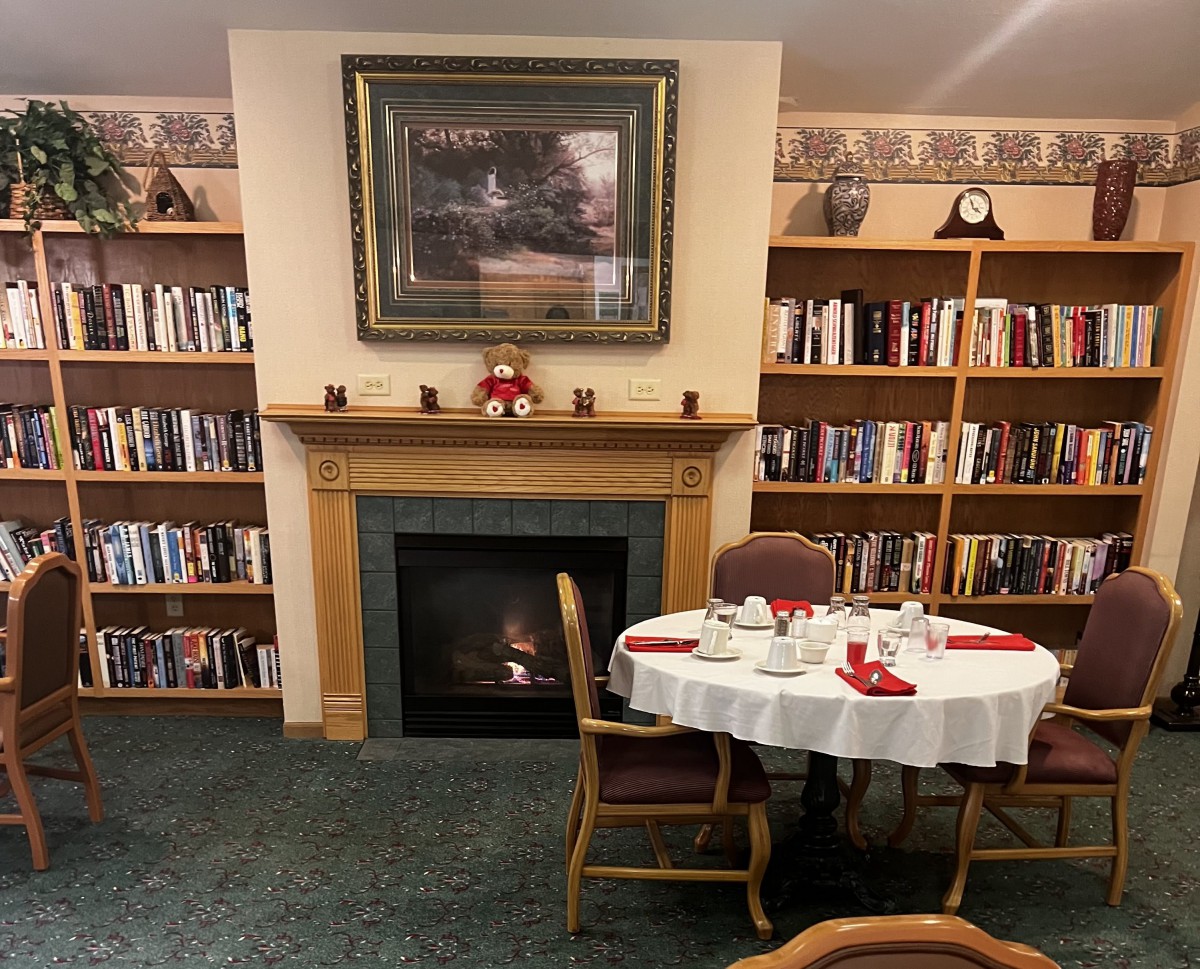 A cozy corner of a library featuring a fireplace surrounded by bookshelves and a set dining table.