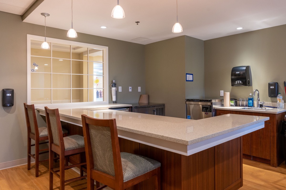 A modern kitchen interior with a dining area, featuring a countertop, chairs, and pendant lighting.