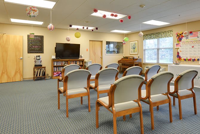 An indoor seating area with rows of chairs facing a television, featuring carpeted flooring and colorful decorations.