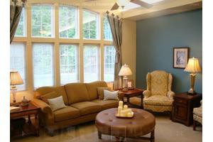 A cozy living room with a large sofa, elegant armchair, and ample natural light from the tall windows.