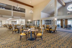 A spacious and elegantly designed dining area featuring multiple tables, cushioned chairs, and decorative chandeliers.