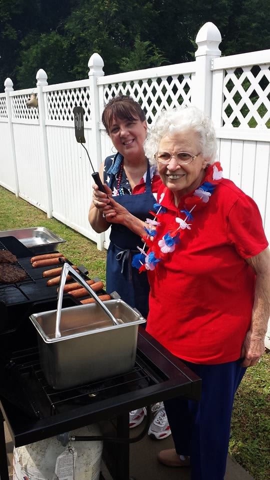 Two women enjoying a barbecue, grilling hot dogs outdoors during a summer celebration.