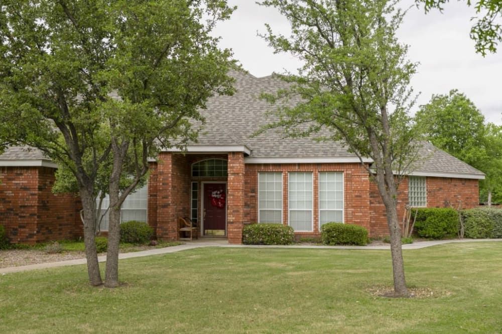 A brick house surrounded by trees and a well-kept lawn.