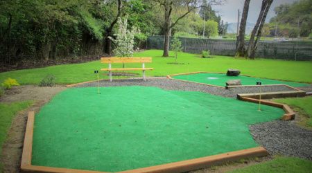 A serene mini golf course surrounded by lush greenery with a park bench in the background.