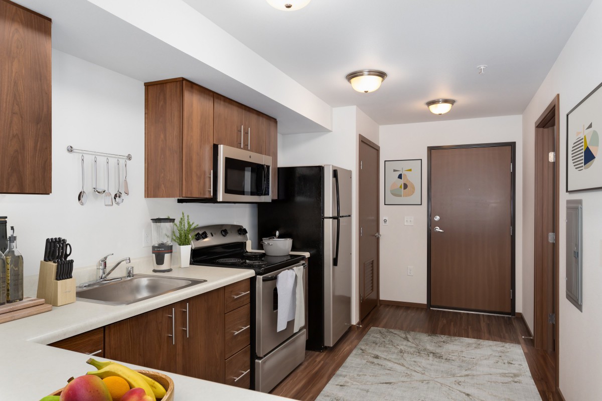 A modern kitchen with wooden cabinets and stainless steel appliances in an apartment setting.