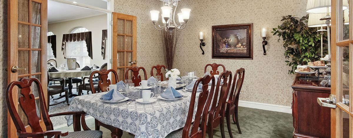 A well-decorated dining room with a full table setting, featuring elegant chairs and a chandelier.