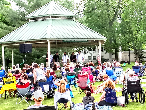 A lively outdoor concert taking place in a gazebo, with a large crowd enjoying the summer day.